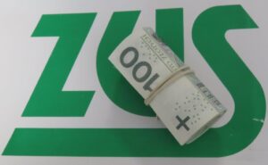 Zdjęcie przedstawia plik banknotów 100 zł na tle logo ZUS